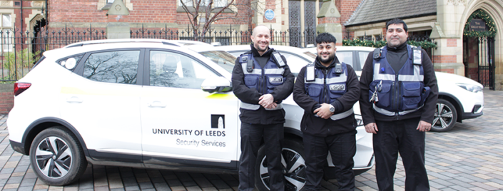 Security Services standing outside the Great Hall building, featuring the electric vehicle