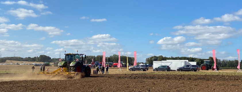 The field at the Research Farm with a tractor ploughing, stands and people are in the background